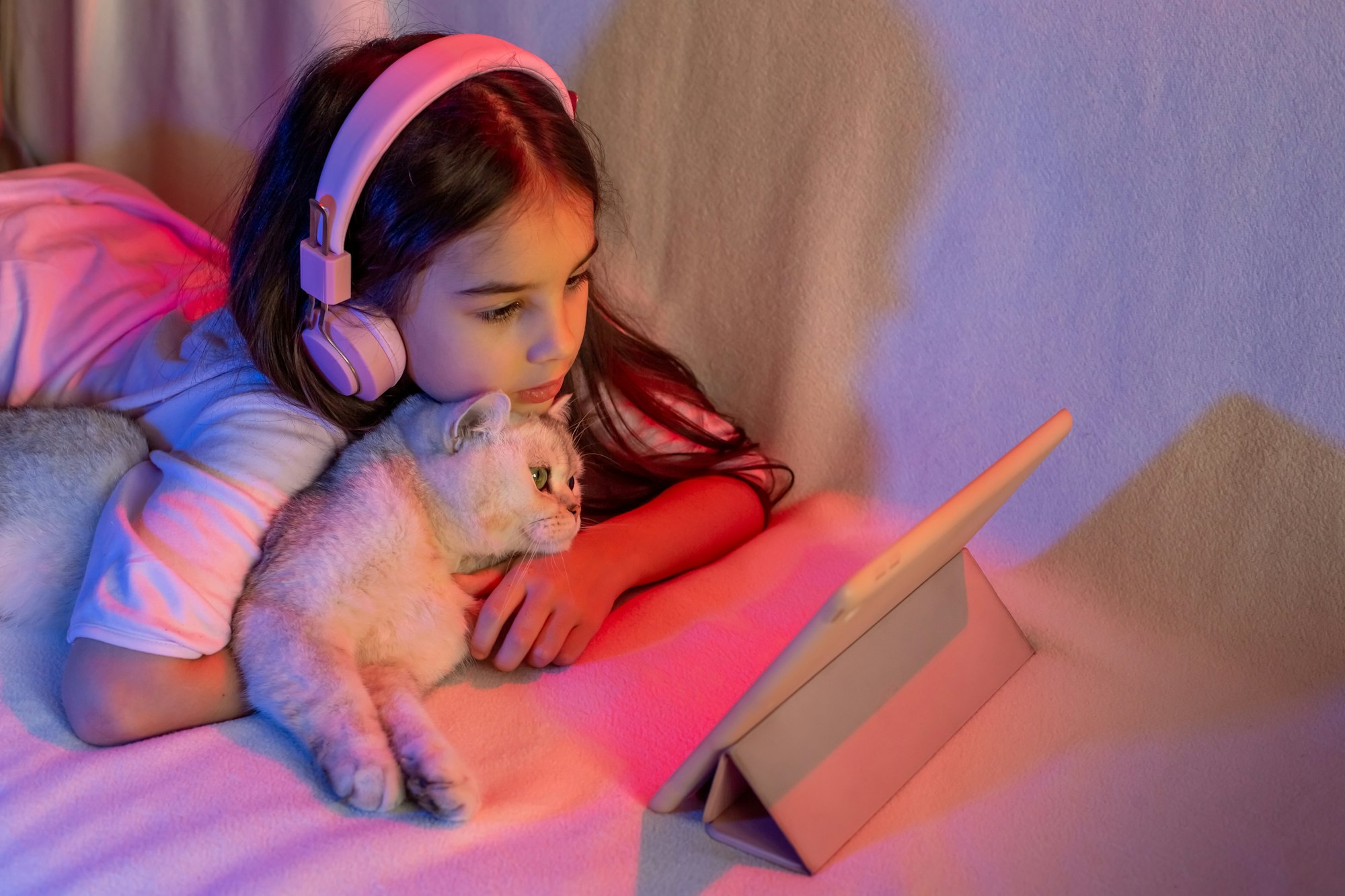 A little girl in pink headphones, with a white adorable cat in neon light